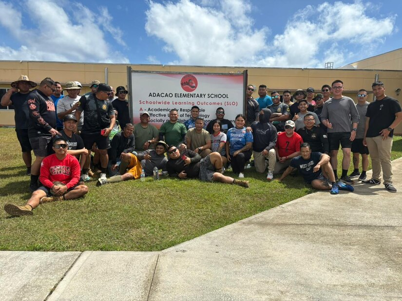 A large group of people take a photo outside of a school.