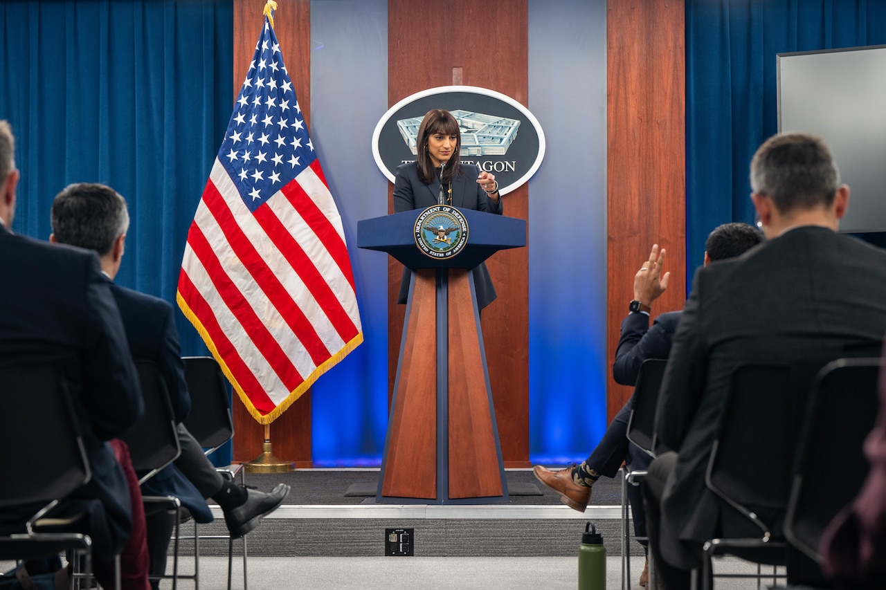 A woman stands behind a lectern. Multiple people are seated in front of her.