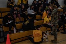 U.S. Marine Corps Lance Cpl. Sarah Grawcock, a combat photographer and mascot handler with Headquarters and Service Battalion, and Pfc. Bruno, the Marine Corps Recruit Depot San Diego and Western Recruiting Region mascot, interact with participants of the "In Their Boots" and "Devil Pups"  events at MCRD San Diego on Feb. 16, 2024. The Devil Pups event is aimed at providing children ages 5-12 with engaging activities that introduce them to aspects of the Marine Corps lifestyle, fostering learning and discipline in a fun environment. (U.S. Marine Corps photo by Sgt. Jesse K. Carter-Powell)