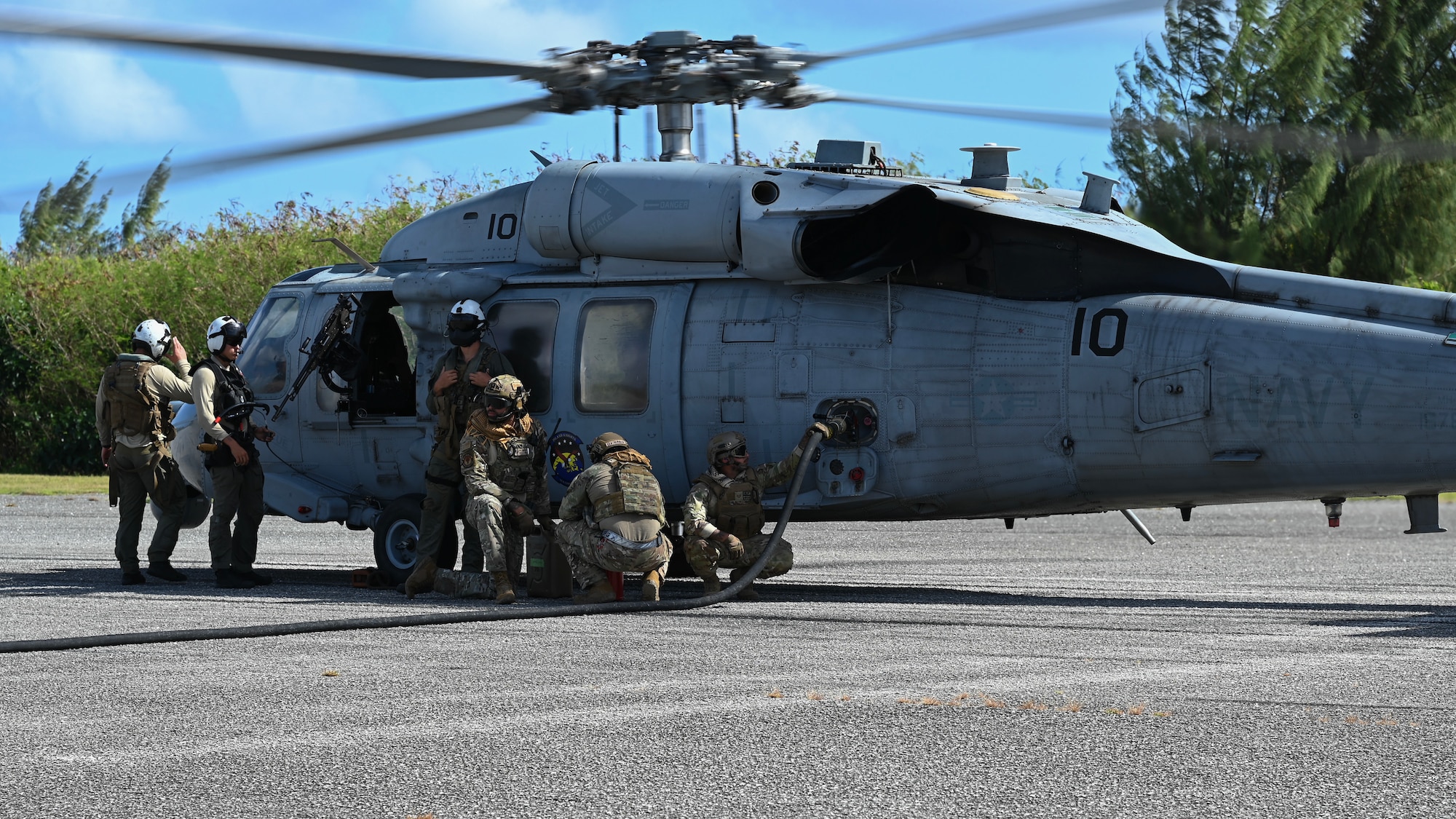 Three Airmen fuel a MH-60 helicopter while three Navy pilots wait for the process to finish.