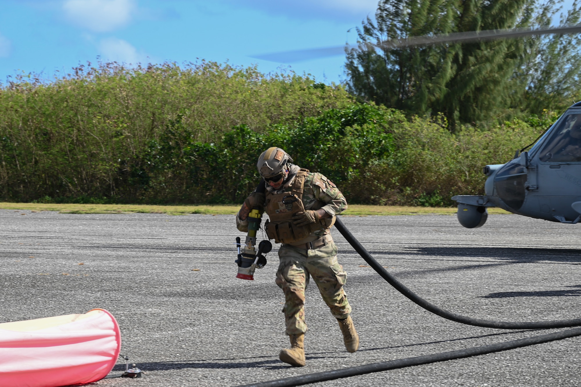 An Airman runs across the airfield with a fuel injection hose on his back.