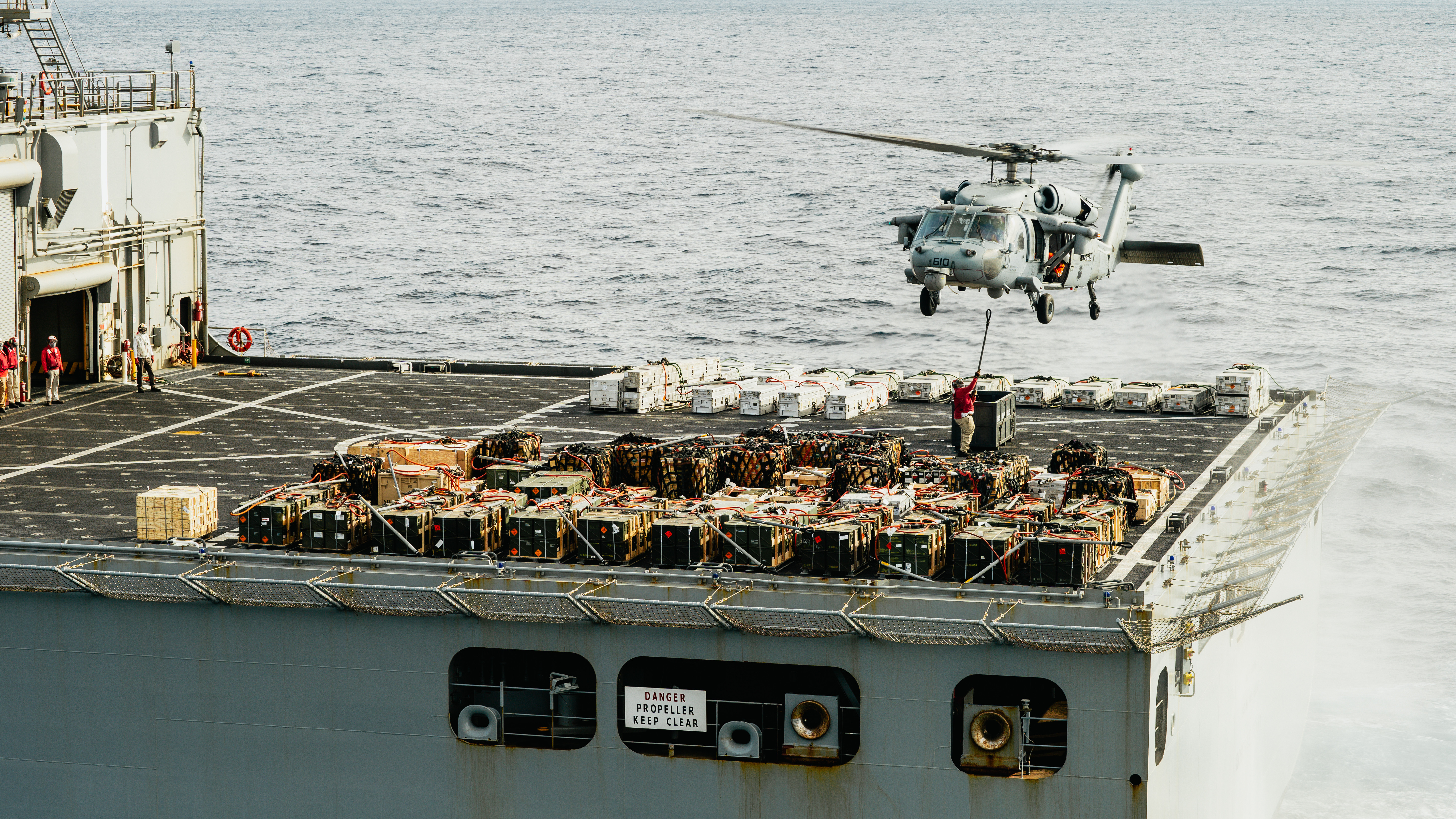 A civil service mariner aboard USNS Robert E. Peary (T-AKE 5) attaches ammunition to an MH-60S Sea Hawk helicopter.