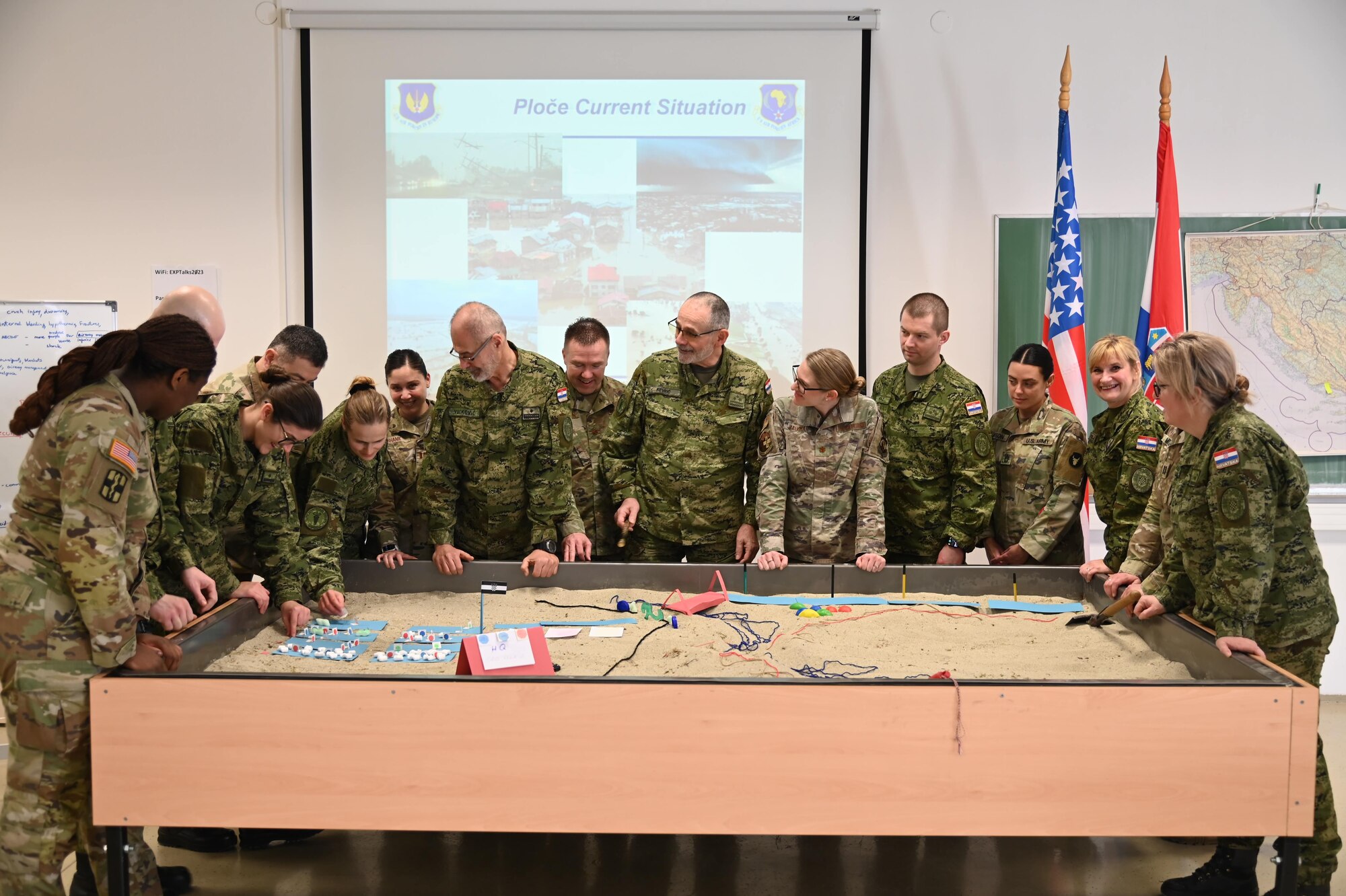 14 uniformed members discuss around a sand diorama table