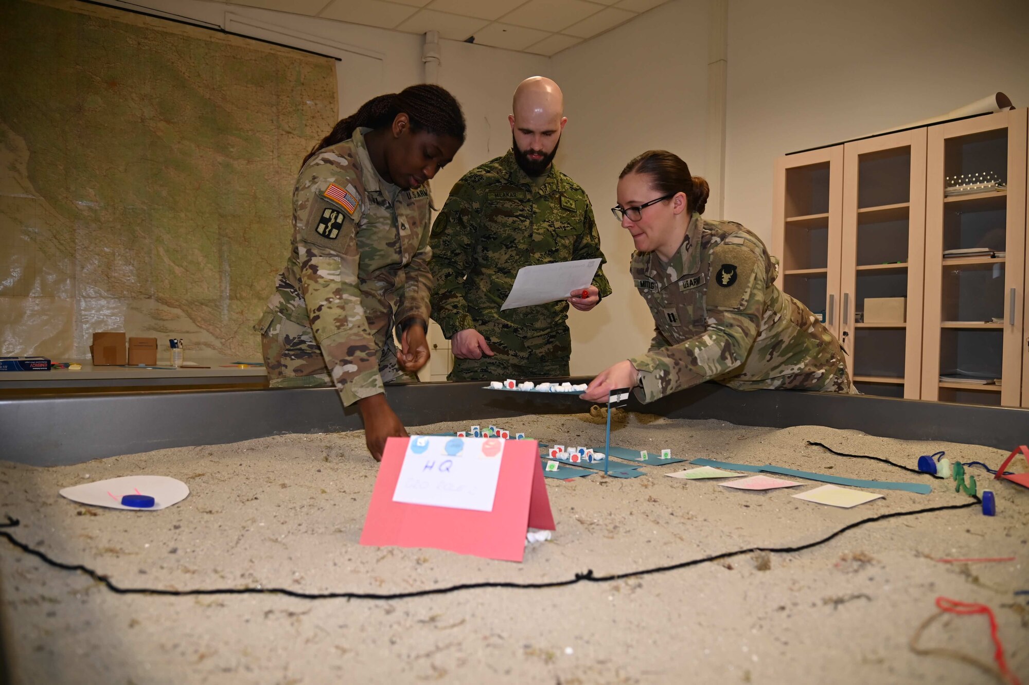 3 uniformed members discuss around a sand diorama table