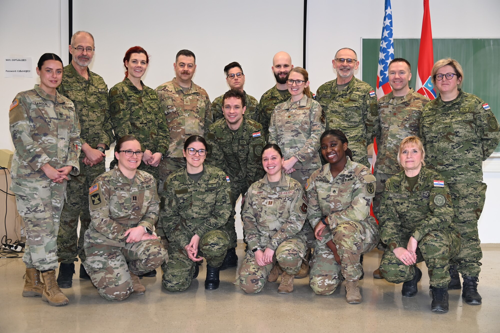 16 uniformed members stand/crouch in formation