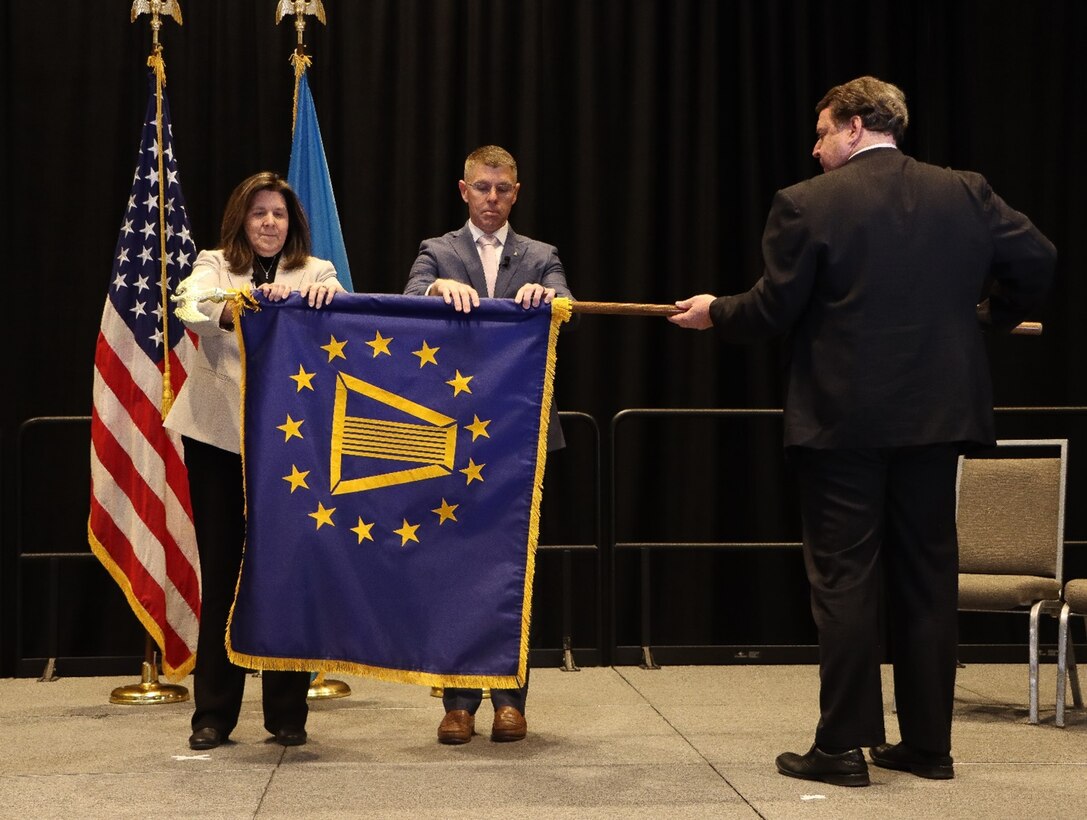 Two people unrolling a blue flag with yellow details while a third person holds the flag horizontally.