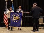 Two people unrolling a blue flag with yellow details while a third person holds the flag horizontally.