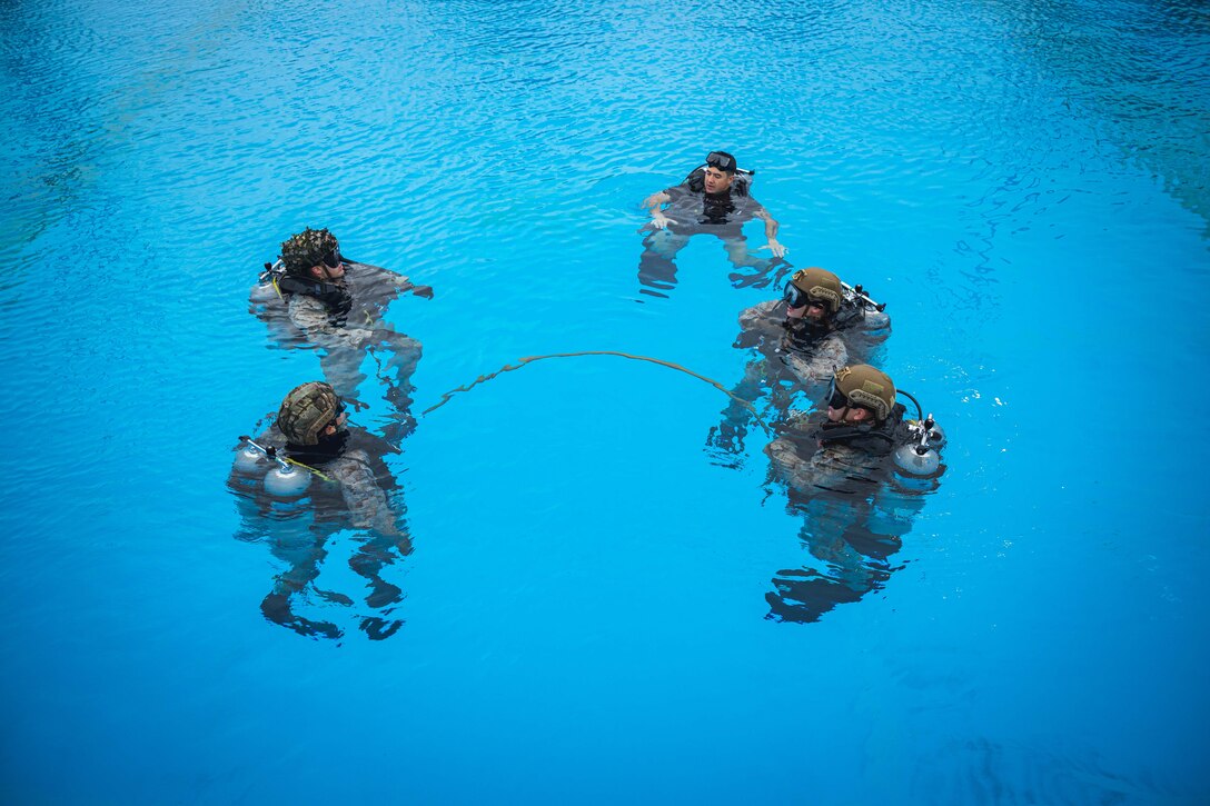 Five Marines with oxygen tanks and goggles tread water in a large pool.