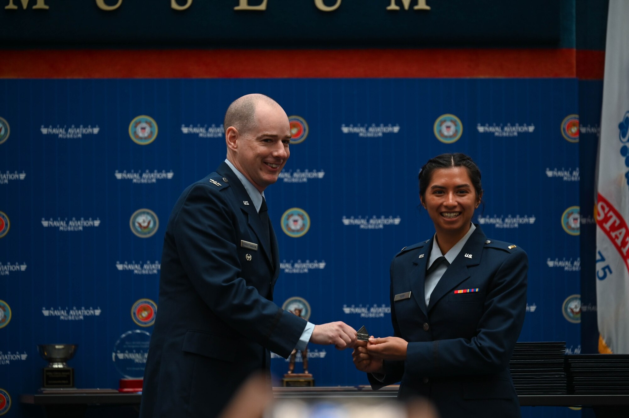 U.S. Air Force Col. John Christianson, 350th Spectrum Warfare Wing deputy commander, left, poses for a photo while presenting the Combat System Operator duty badge to U.S. Air Force 2nd Lieutenant Mary Kemp, 479th Flying Training Group graduate, right, during the Undergraduate Combat Systems Officers Course graduation ceremony at the National Naval Aviation Museum, Naval Air Station Pensacola, Fla., Feb. 16, 2024. Combat System Operators abstract key environmental information and employ a wide range of high-tech systems and weaponry in the air to provide the precision needed to carry out increasingly complex missions.(U.S. Air Force photo by Capt. Benjamin Aronson)