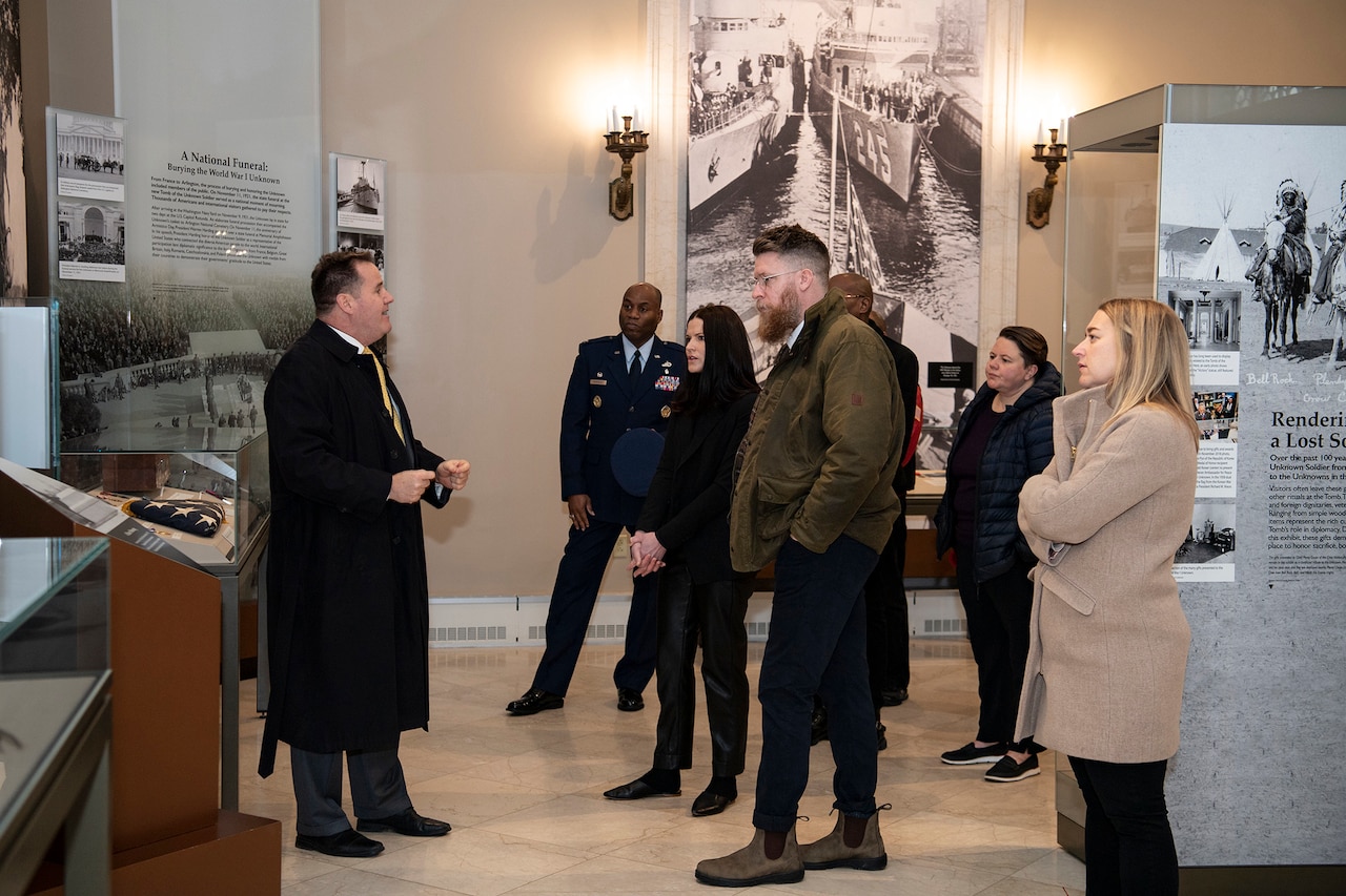 A group of people stand and listen as a person speaks.