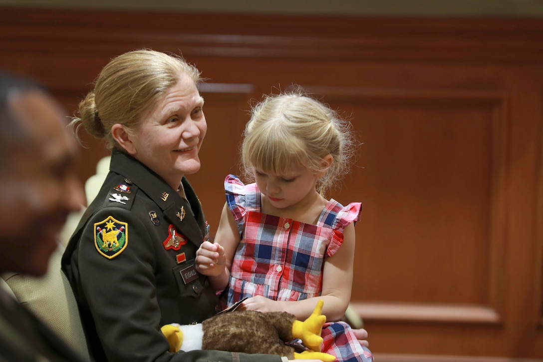 A child playing with a stuffed animal sits on a soldier’s lap during a ceremony.