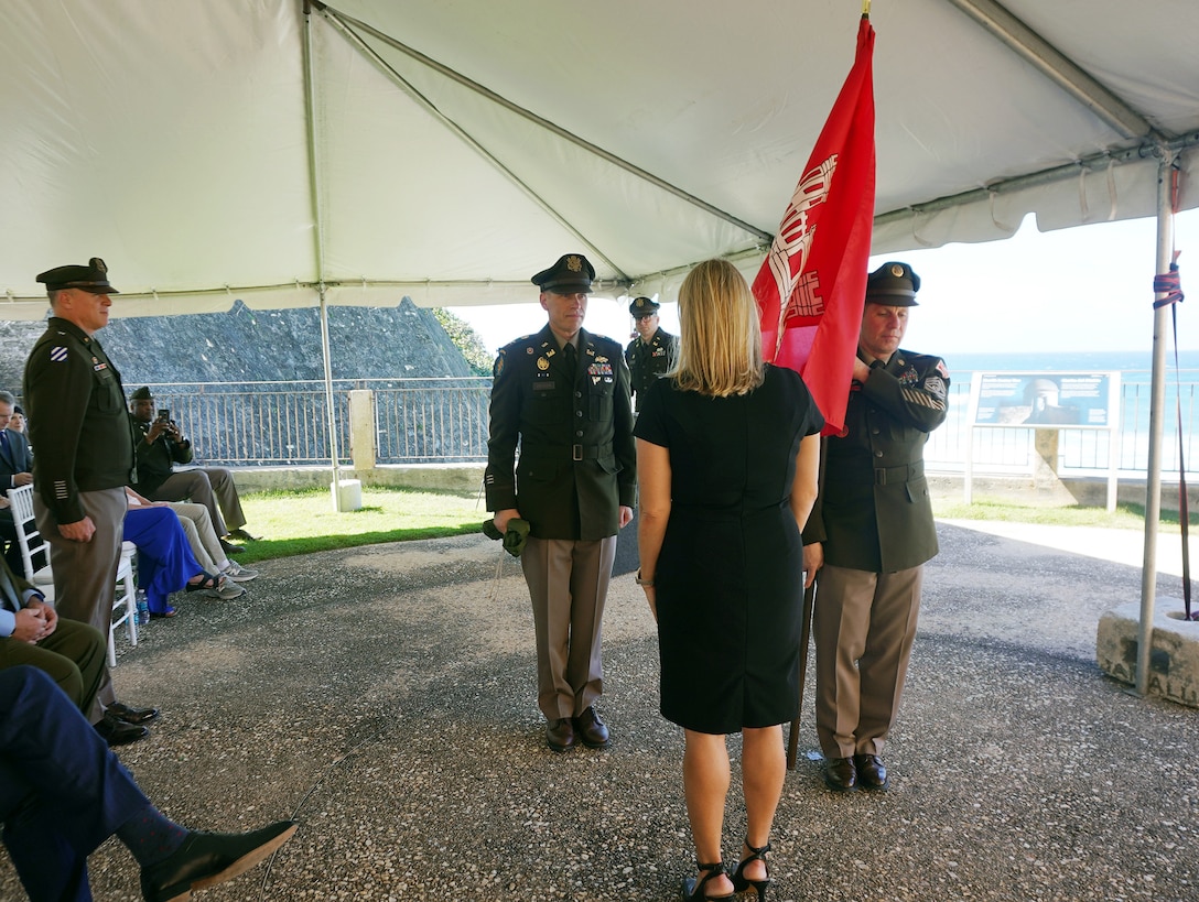 Brig. Gen. Daniel Hibner, Col. Charles Decker, Jacqueline Keizer U.S. Army Corps of Engineer,  Cmd. Sgt. Maj. Rodney C. Russell (with red USACE flag) standing under a tent before a seated audience.