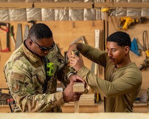 Two Airmen use power tools to screw together pieces of wood while building a desk.