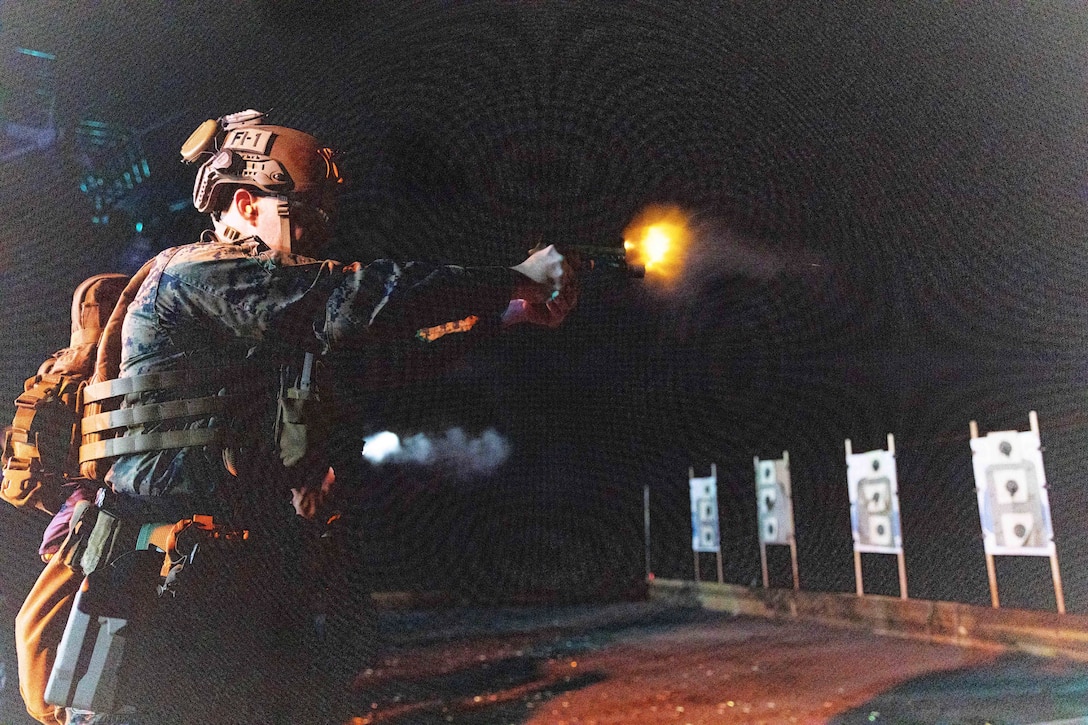 A Marine fires a weapon at a target during weapons training in the dark on a ship's deck.