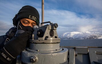 QM3 Kaevon Dutchatellier looks through an alidade on the bridgewing as USS Gunston Hall (LSD 44) arrives in Harstad, Norway.