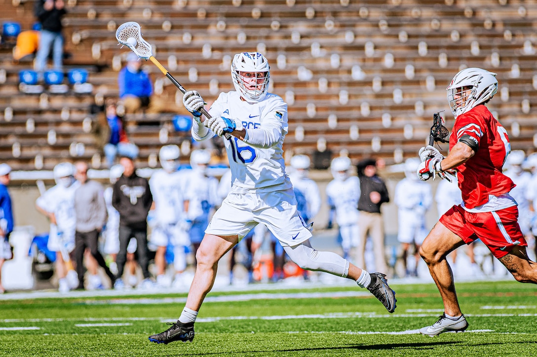 A lacrosse player prepares to pass a ball during a match as an opponent approaches.