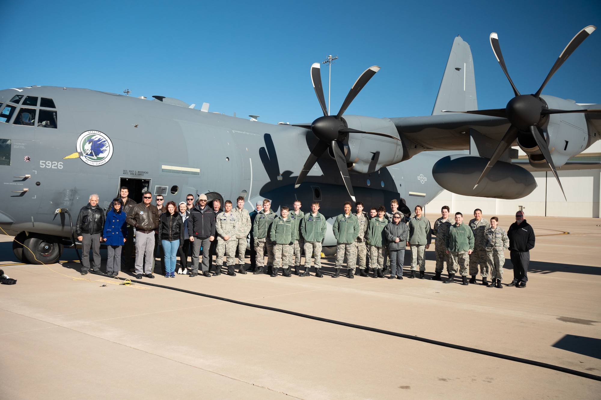 A group of young adults and adults in military uniform stand in front of a military aircraft for a group photo.