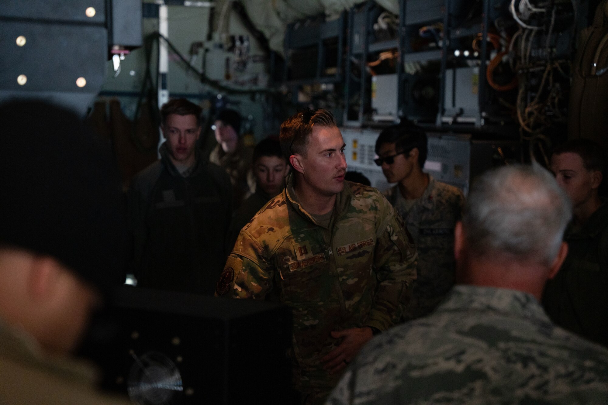 A man in military uniform speaks to a group of people in military uniform inside a military aircraft.