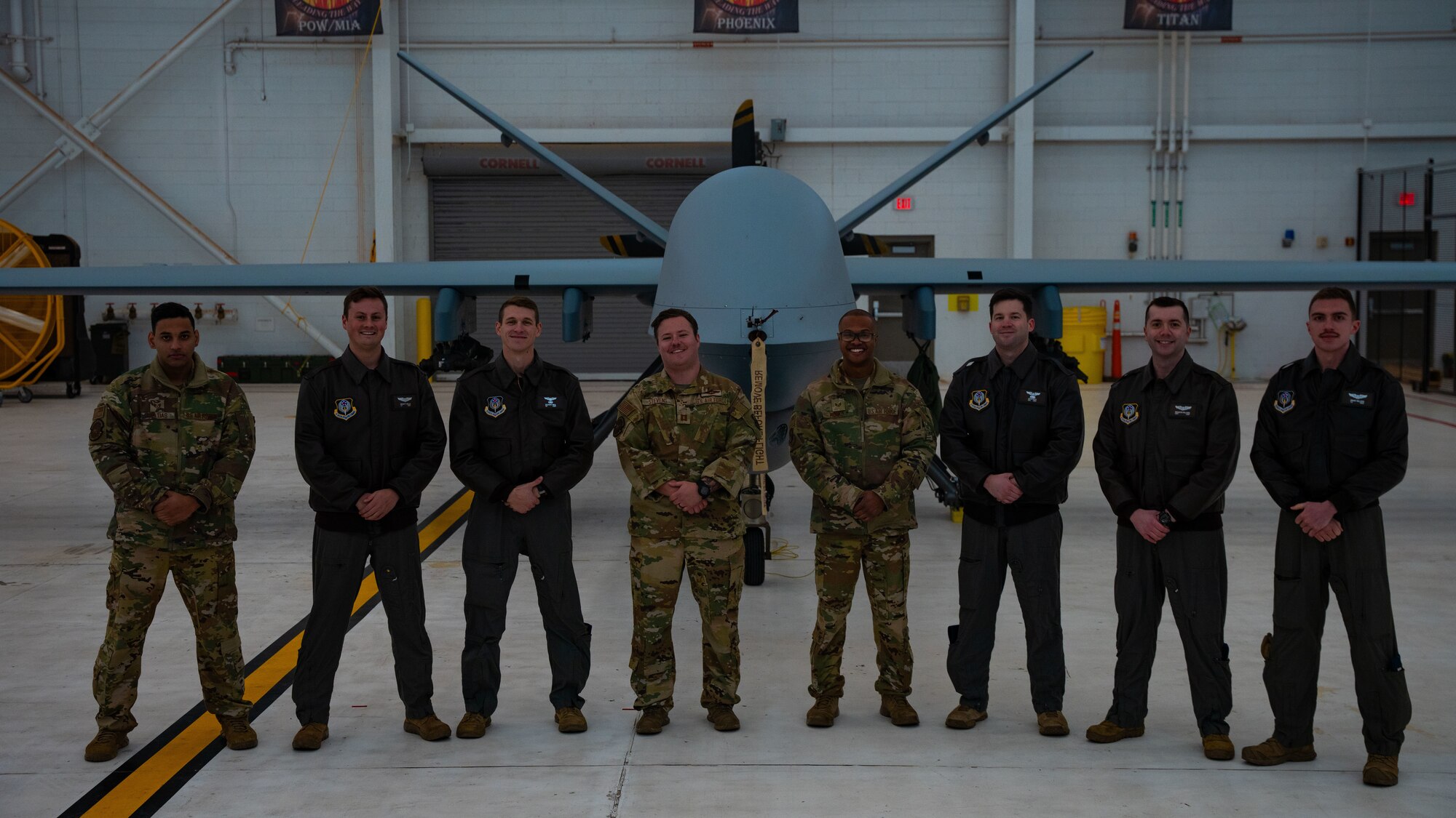 A group of eight people in military uniform stand in front of a military aircraft for a photo inside an aircraft hangar.