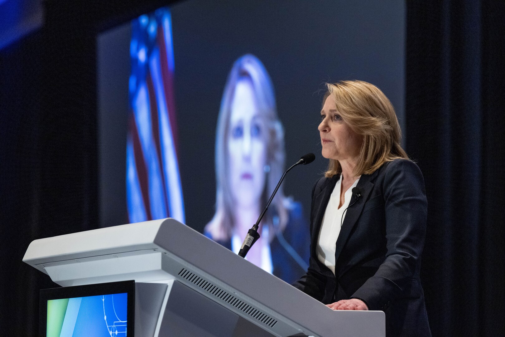 A civilian speaks to a crowd from a lectern.