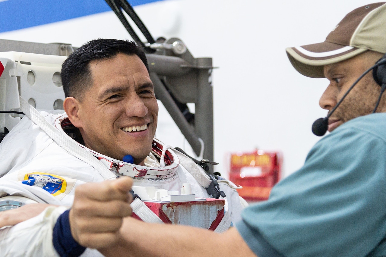 An astronaut gets help putting on a spacesuit.