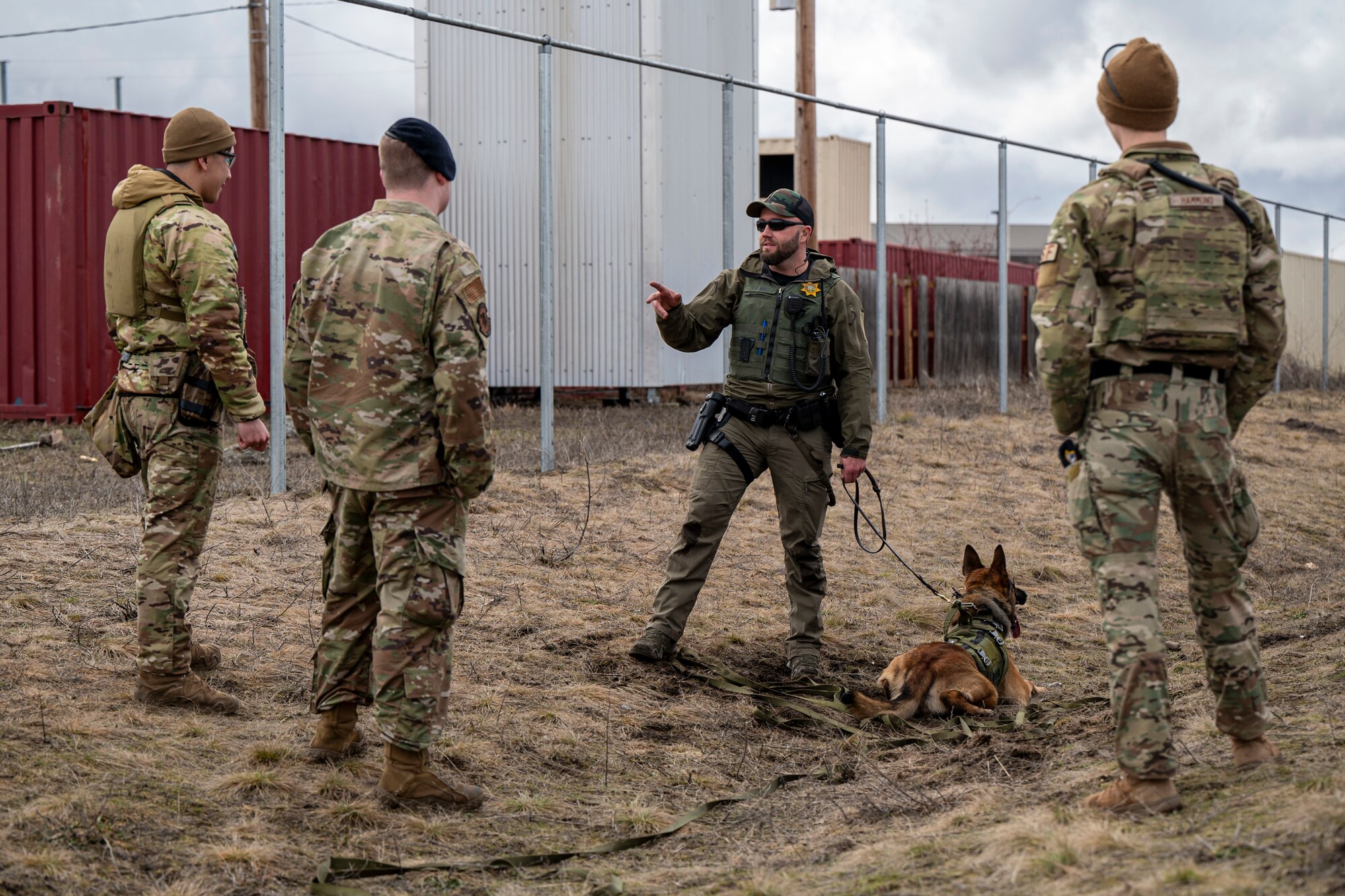 Four people and a K-9 dog stand in a circle and talk