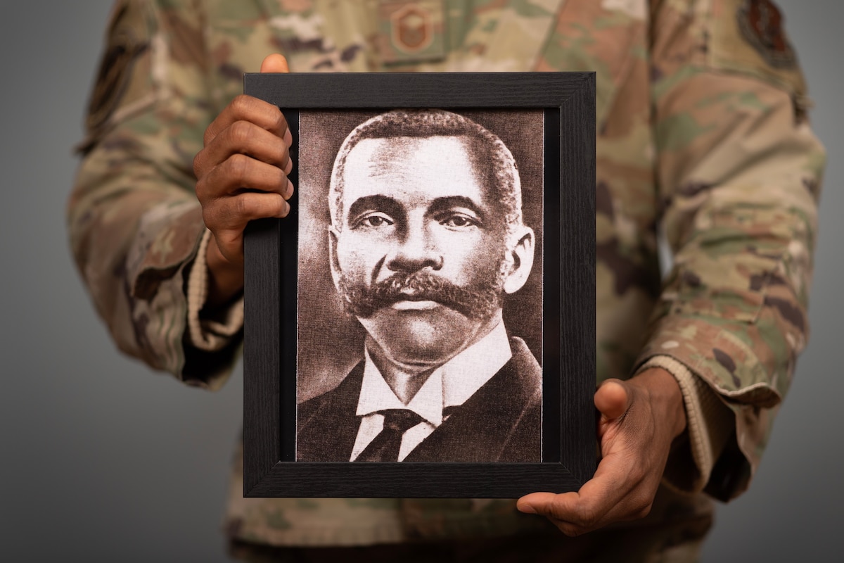 Photo of U.S. Air Force Master Sgt. Juan J. Coleman, 158th Fighter Wing traffic management specialist, holding a photograph of his great-great-great grandfather, Rev. Joe Berry Powell, at the Vermont Air National Guard Base, Feb. 21, 2024.