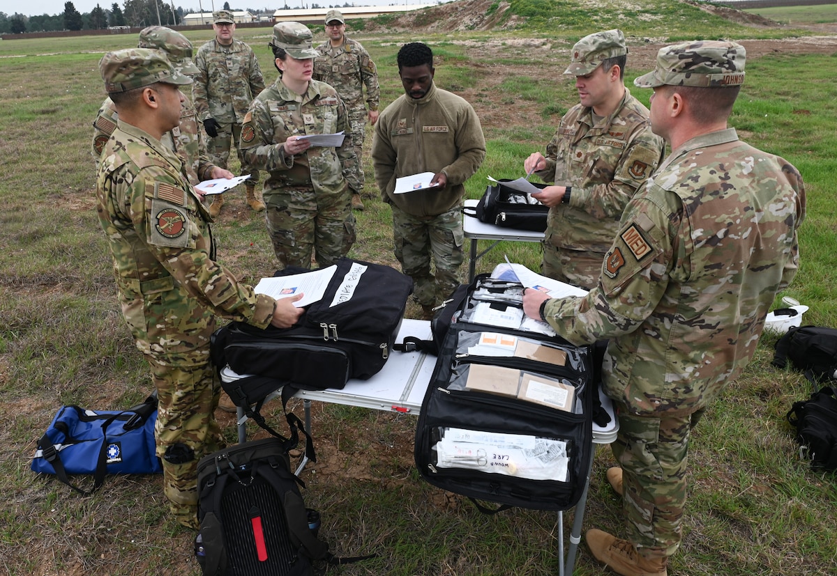 Six members of the 39th Medical Group are gathered in a circle around a table in a field conducting equipment inventories and discuss their training scenarios during a contingency exercise.