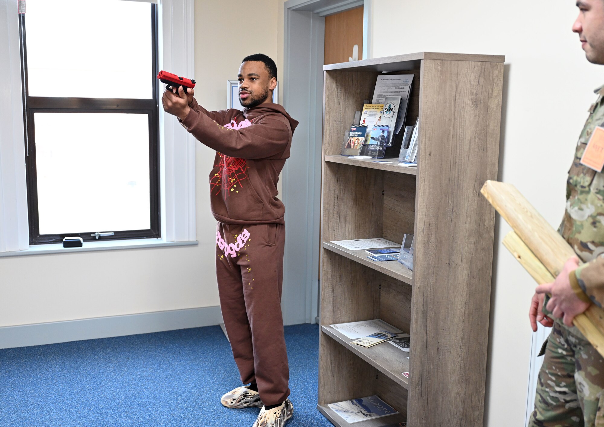 U.S. Air Force Senior Airman Kesean Wilson, left, 100th Security Forces Squadron response force leader, role-plays as an active shooter as another 100th SFS member gets ready to bang together pieces of wood to simulate gunshots during an exercise at Royal Air Force Mildenhall, England, Feb. 15, 2024. Airmen from the 100th SFS and 100th Civil Engineer Squadron responded to the exercise scenario, which was designed to evaluate the training, readiness and capability of RAF Mildenhall first responders to effectively respond to active shooter threats on the installation. (U.S. Air Force photo by Karen Abeyasekere)