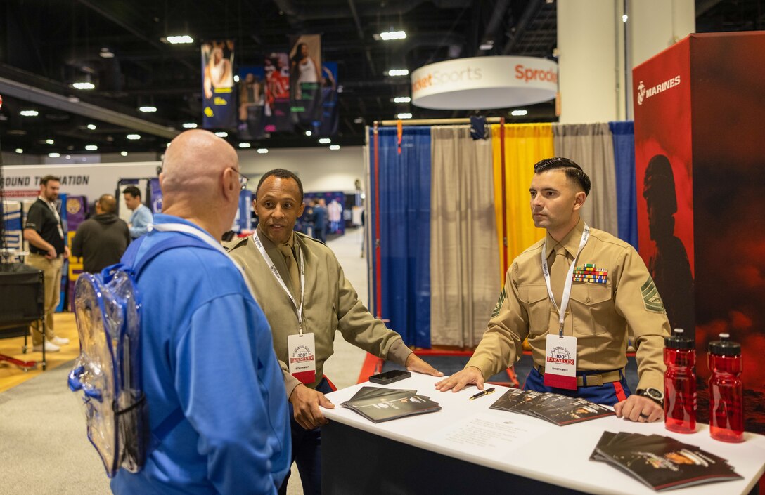 U.S. Marine Corps Capt. Aaron Webster, national partnership officer with Marine Corps recruiting command, center, and Gunnery Sgt. Edwin Omanahernandez, senior enlisted advisor of the Martial Arts Fitness Center of Excellence on Marine Corps Base Quantico, right speaks with a volleyball coach during the American Volleyball Coaches Association convention, in Tampa, Fla., on Dec. 14, 2023, about the Marine Corps Recruiting Command’s Coaches Workshop. The Marine Corps National Partnerships ensure the coaches of the next generation of Marines have the resources and skills to accurately present the Marine Corps as an option to their athletes, and support recruiter access to prospective audiences. (U.S. Marine Corps Photo by Lance Cpl. Payton Goodrich)