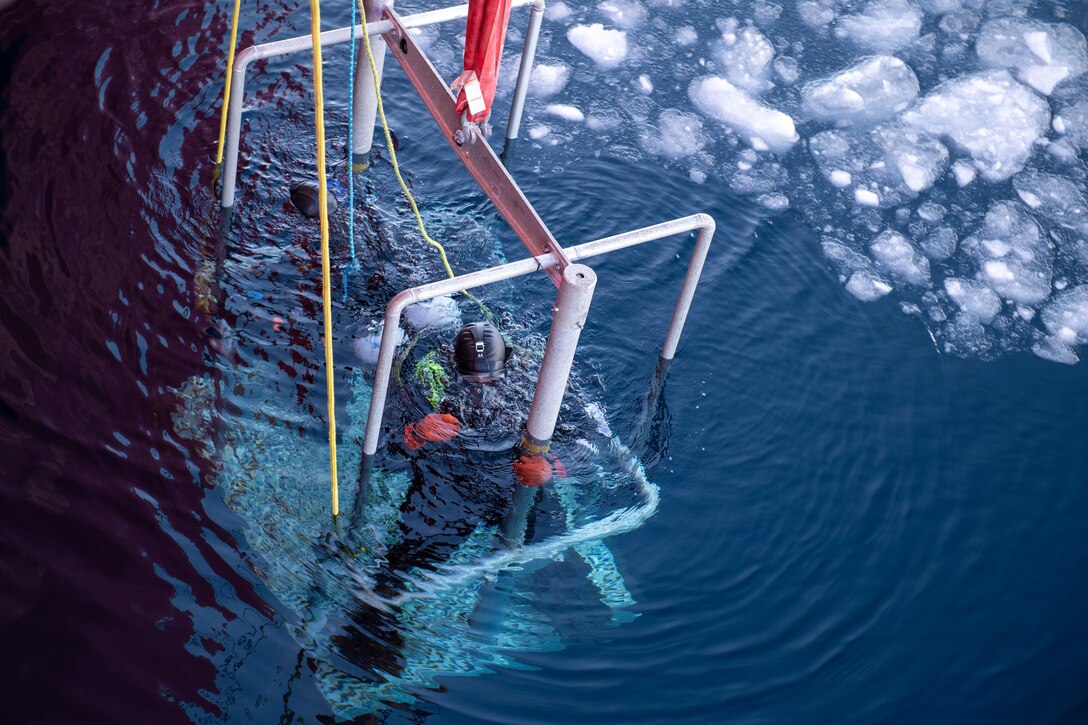 Two Coast Guardsmen wearing wetsuits are lowered on a platform into icy waters.
