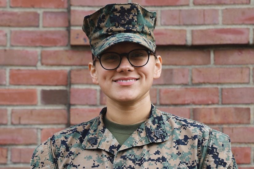A Marine in uniform smiles for a photo while standing in front of a brick wall.