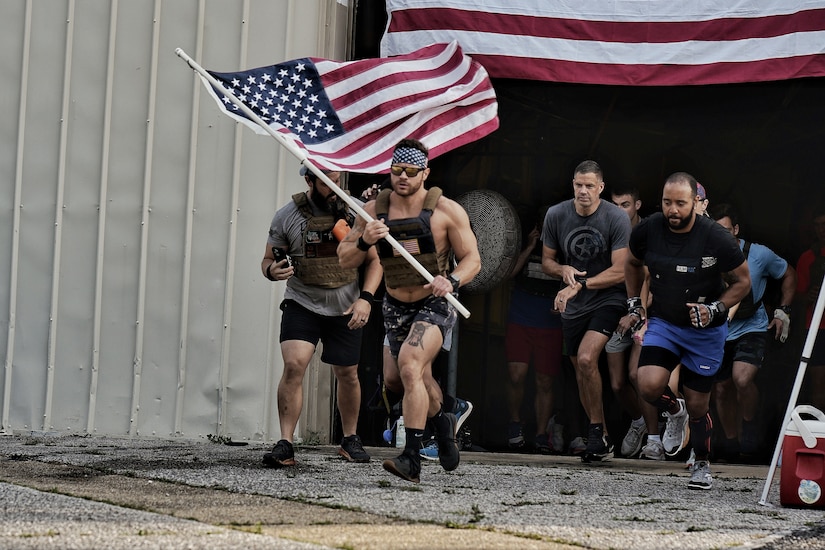 A soldier carrying an America flag leads a group of service members on a run.