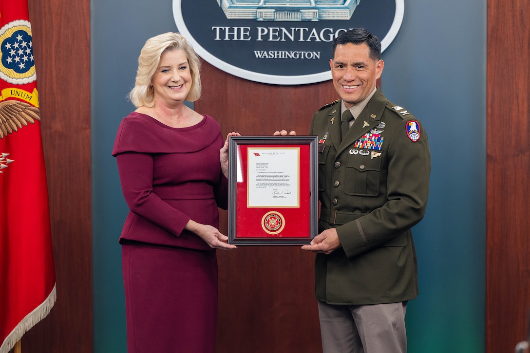 A civilian and a soldier smile while jointly holding up a certificate.