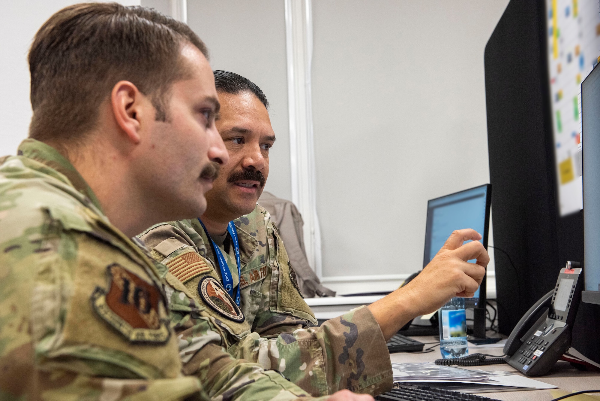 Two Airmen talk while looking at a computer.