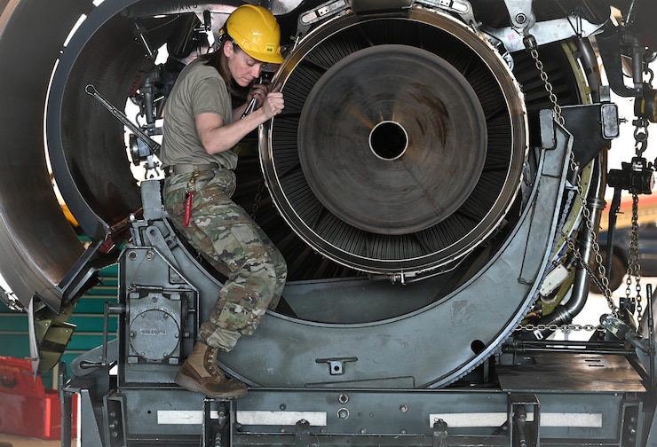 Female Airman in hard hat, positioning engine components.