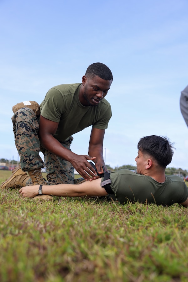 U.S. Marines Corps Sgt. Kendell Jones, the manpower clerk stationed on Marine Corps Base (MCB) Camp Blaz, applies a tourniquet to Cpl. Enrique Sandoval, a food service specialist with MCB Camp Blaz, during a Tactical Combat Casualty Care (TCCC) course on MCB Camp Blaz, Guam, Feb. 22, 2024. TCCC is a joint standardized certification being implemented within the Marine Corps to provide non-medical personnel with the medical skills necessary to ensure lifesaving treatment can be rendered in the absence of a Corpsman and improve the survivability of those wounded or injured in combat. (U.S. Marine Corps photo by Lance Cpl. Ryan Little)