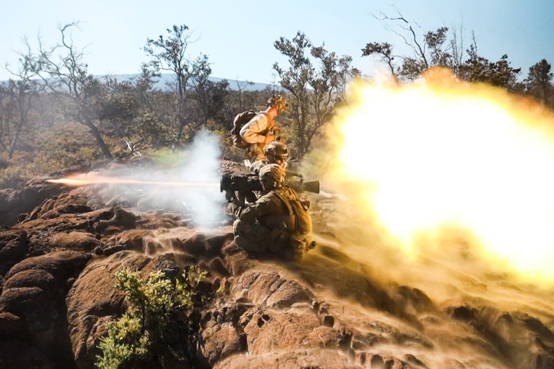 Marines fire a weapon emitting a large cloud of white smoke.