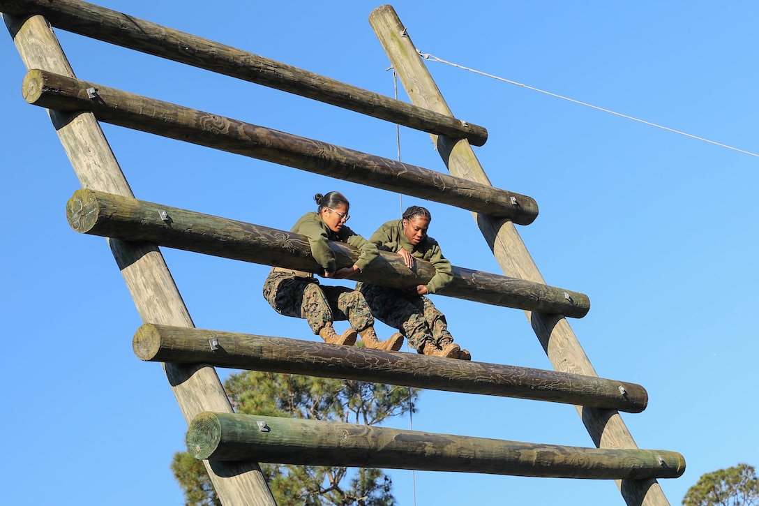 Two Marine Corps recruits climb a wooden obstacle course.