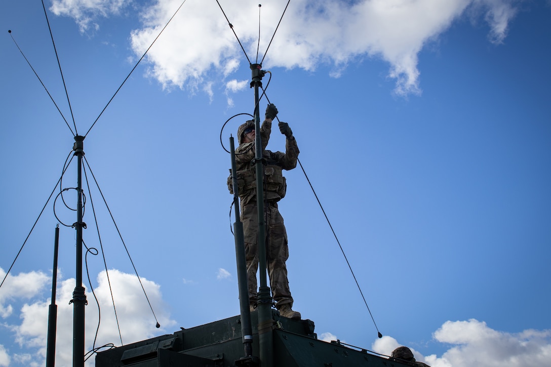 A soldier stands atop a military vehicle to disconnect antennas.