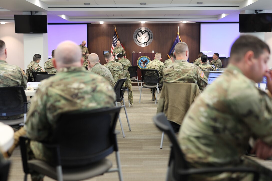 group of men and women wearing u.s. army uniforms sitting at tables with computers in a conference room.