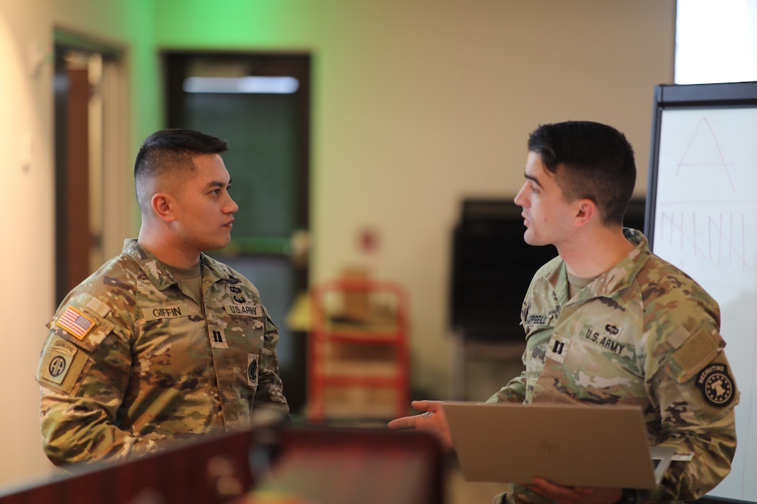 two men wearing u.s. army uniforms standing at the front of the group talking to each other.