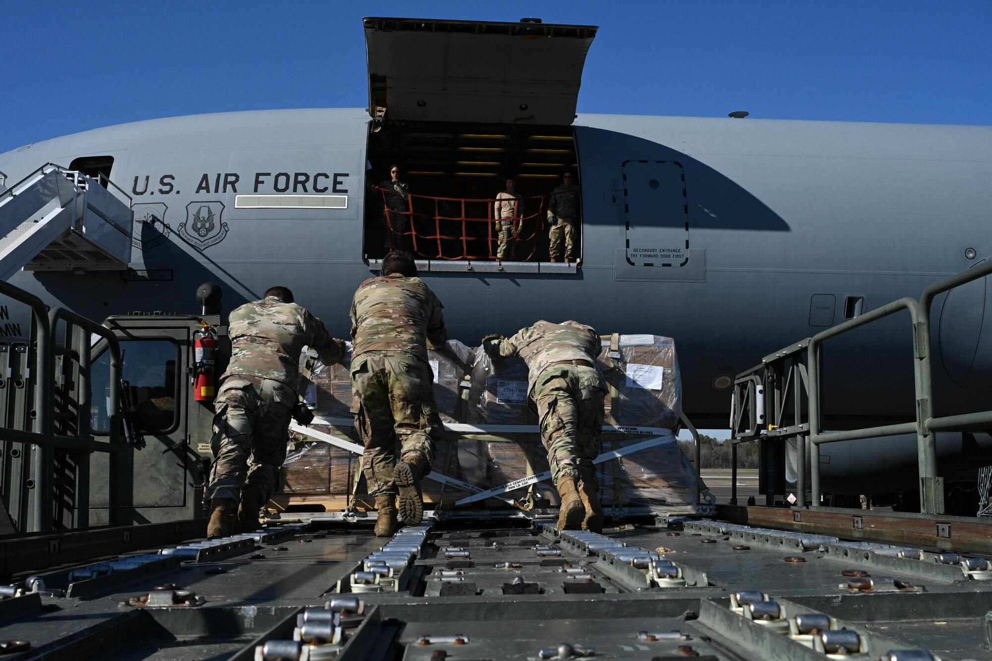 Men in uniform push cargo towards a plane