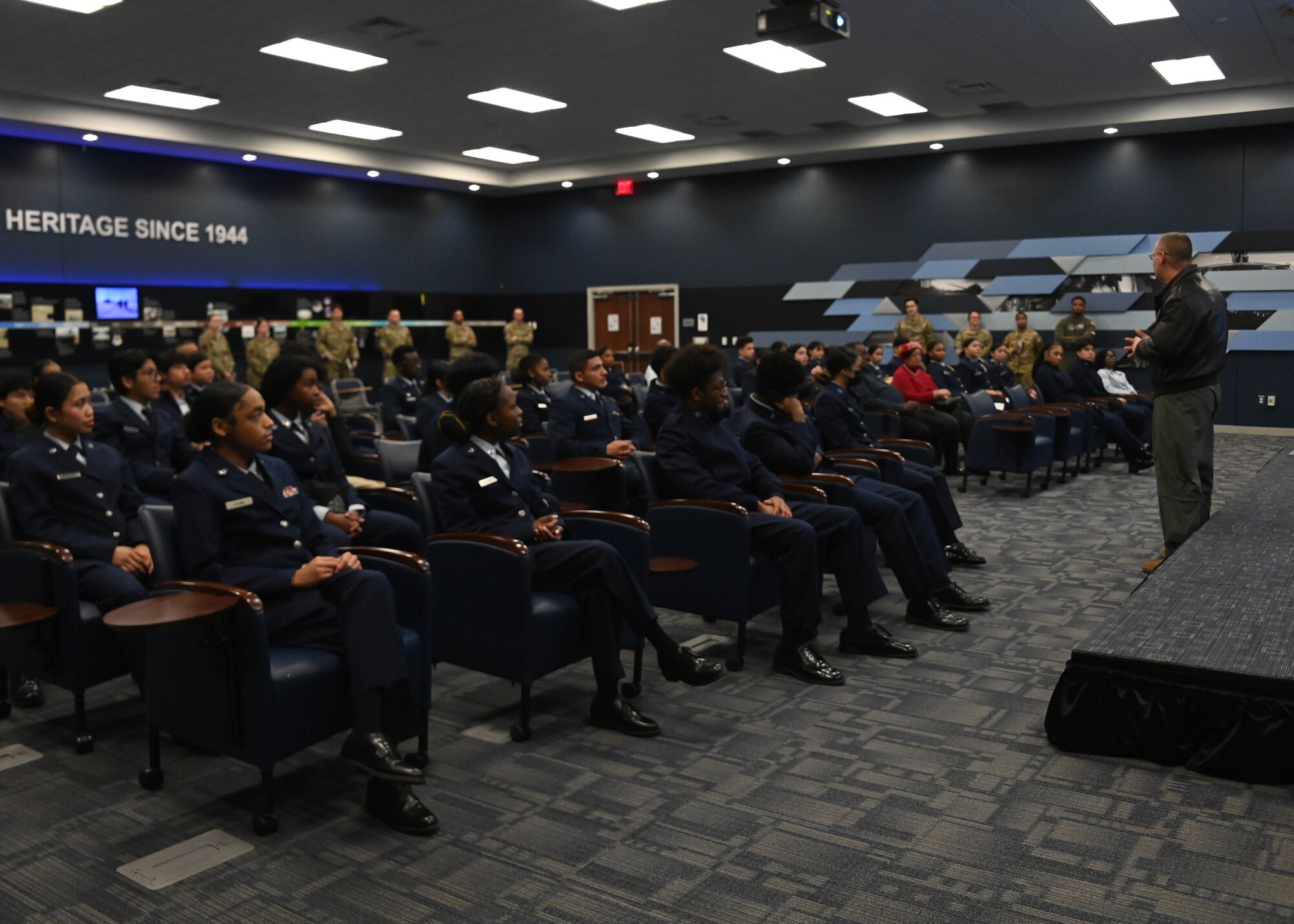 Man stands in front of a large group of students sitting in chairs.