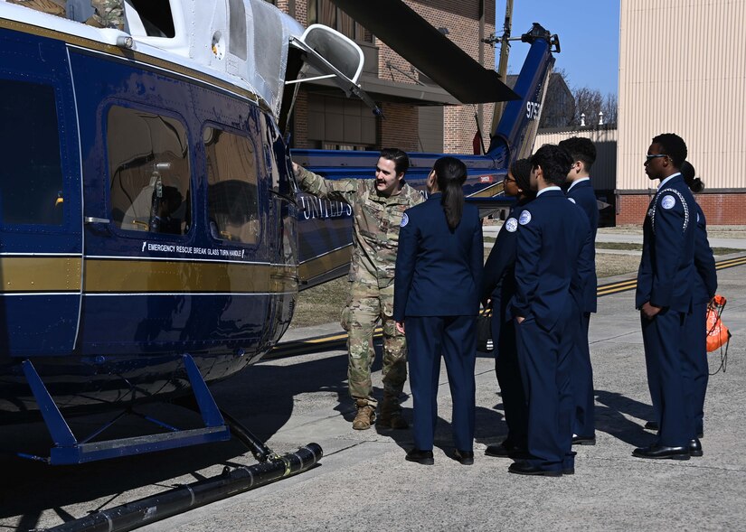 A man points to part of a helicopter in front of a group of high school students.