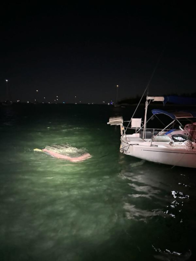 A sailboat is tied to a capsized dinghy