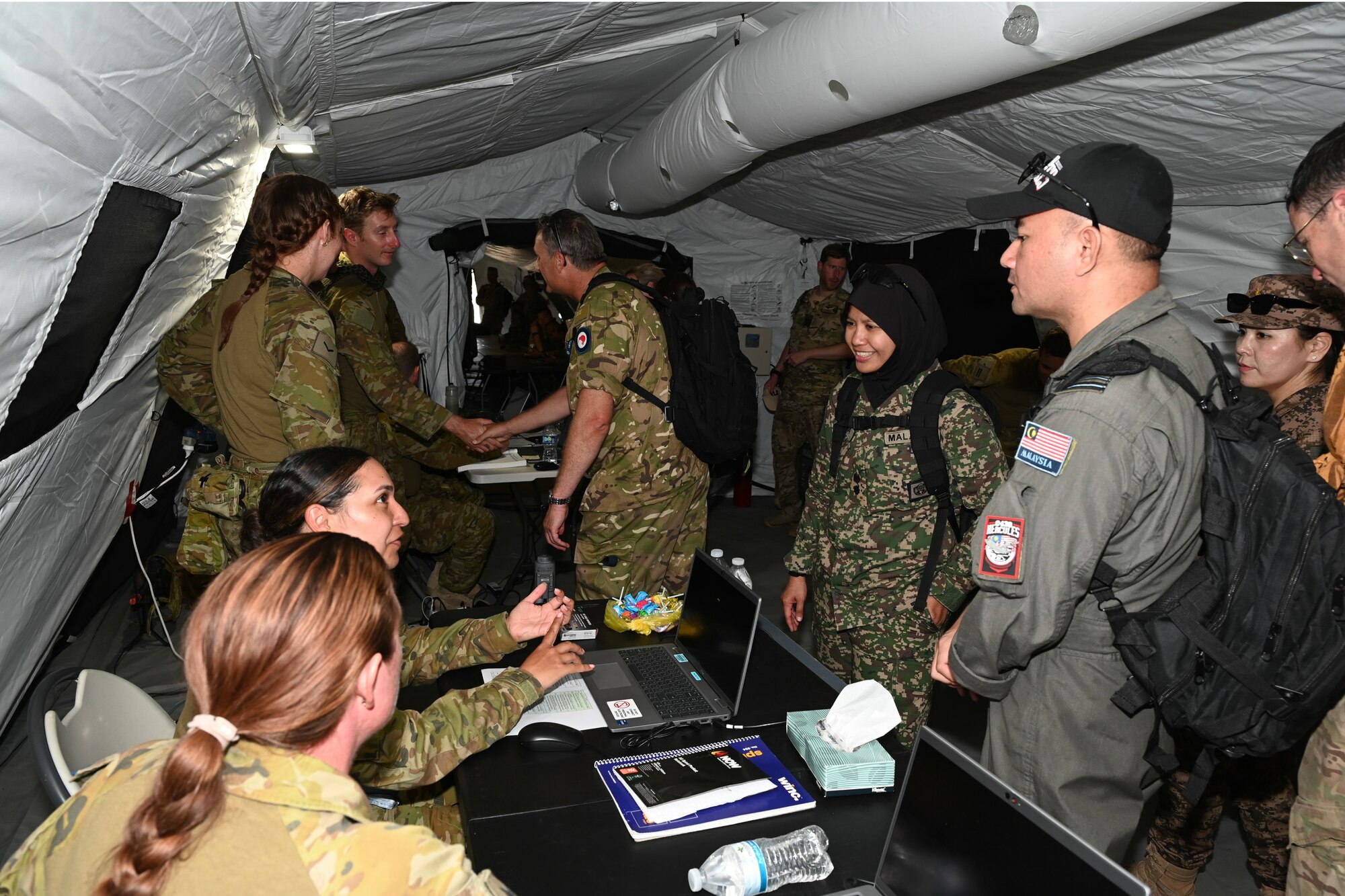 Military members from several countries interact inside of a large tent.