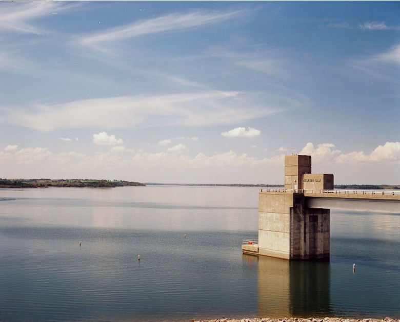 A concrete structure sits in the middle of a lake with a cloudy sky in the background.