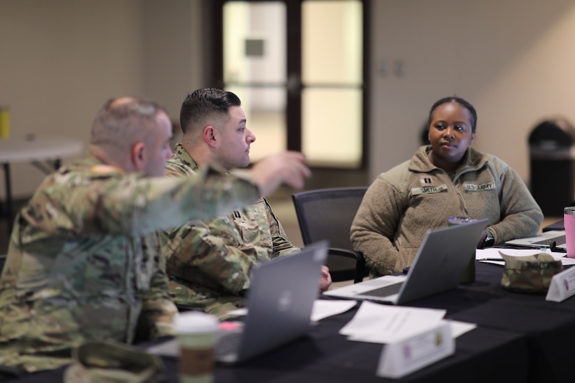 two men and one woman wearing u.s. army uniforms converse at a table with computers.