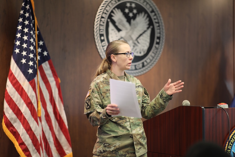 woman wearing u.s. army uniform stands by podium, giving a speech.